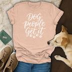 Peach t-shirt with "Dog people Get it" text and paw prints, near a dog.