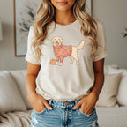 Golden Retriever wearing a pumpkin sweater next to a pumpkin on a cream t-shirt.