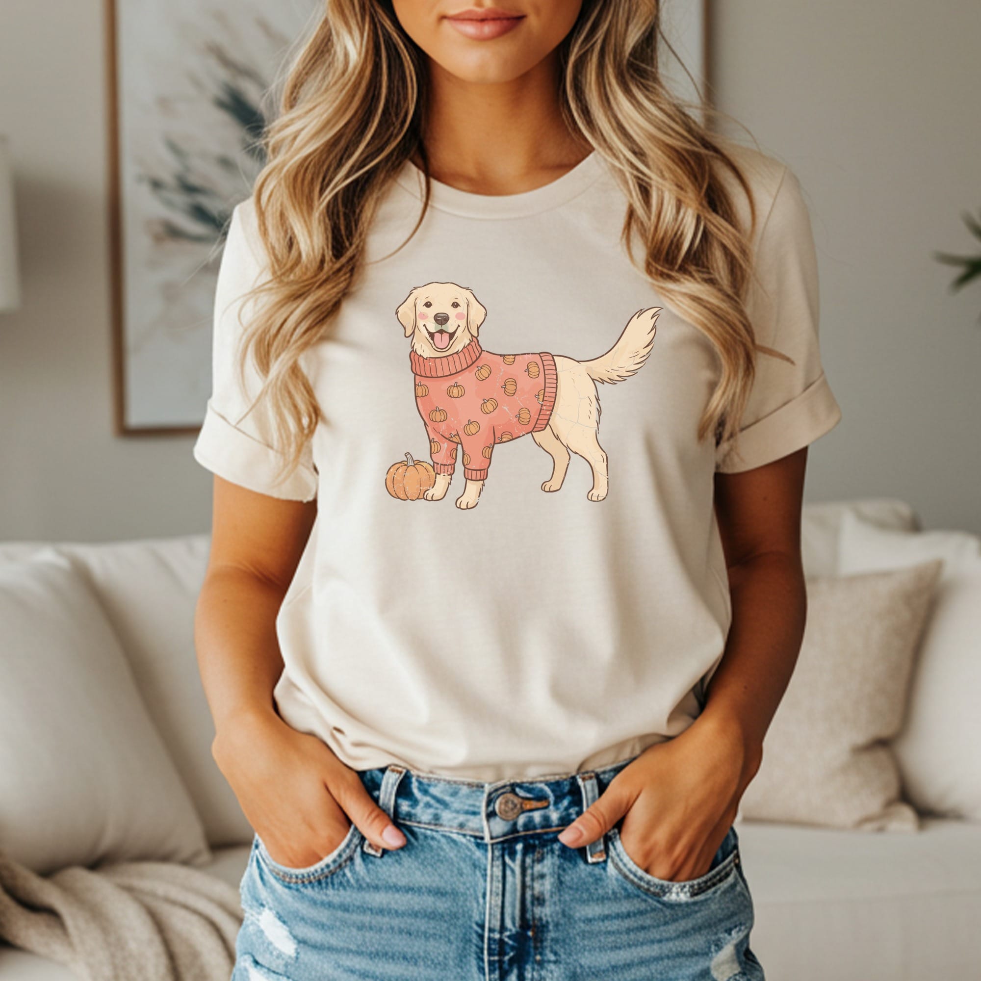 Golden Retriever wearing a pumpkin sweater next to a pumpkin on a cream t-shirt.