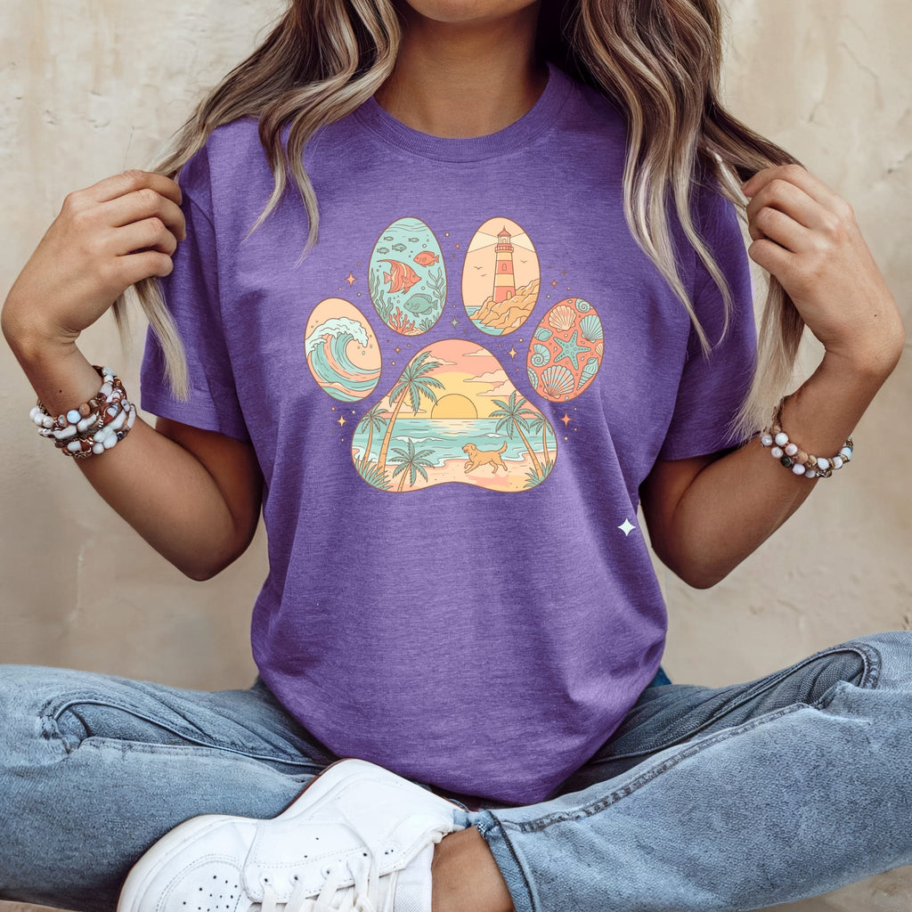 Purple t-shirt with paw print design featuring beach, ocean, and lighthouse scenes.