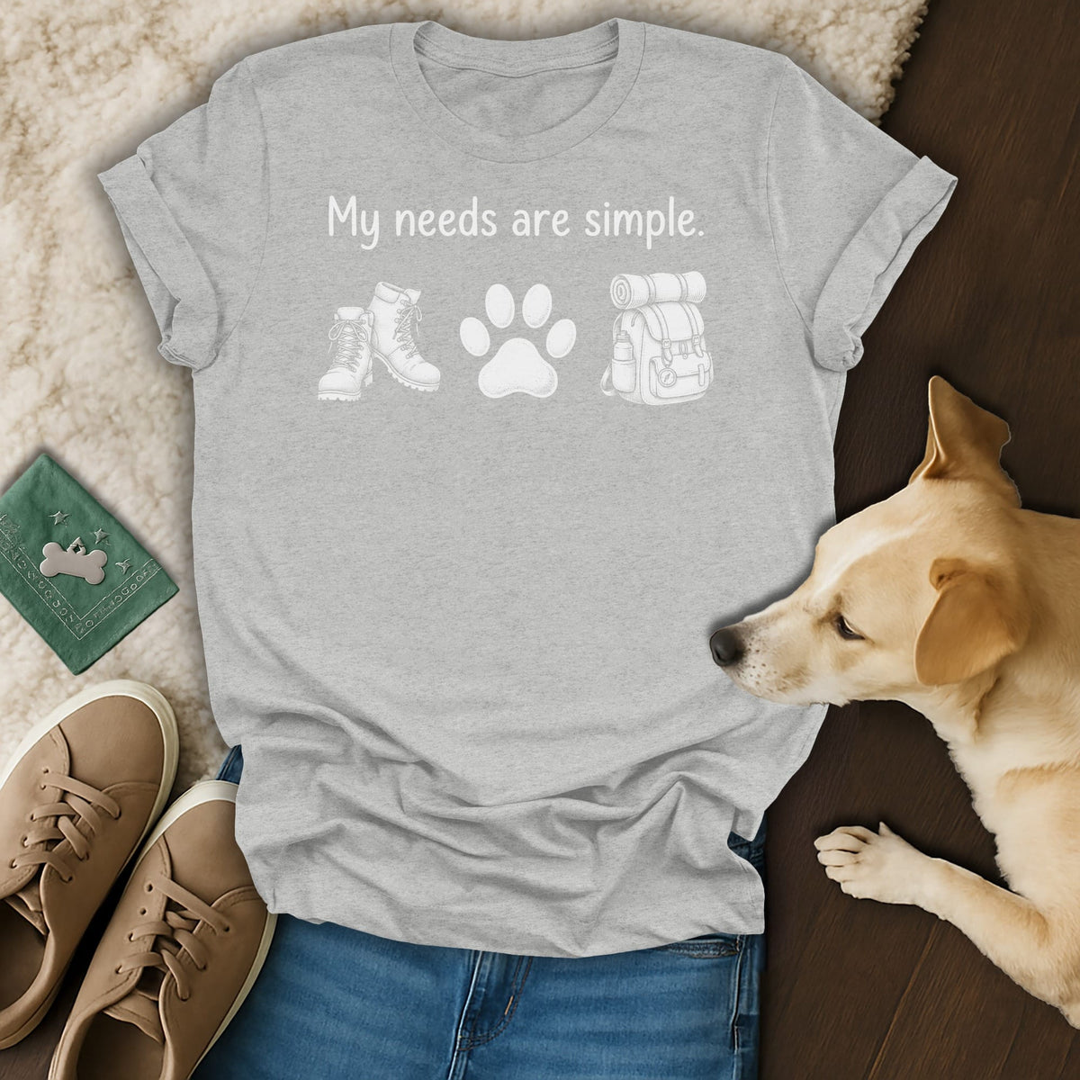 Grey t-shirt with "My needs are simple." text, hiking boots, paw print, and backpack graphic.