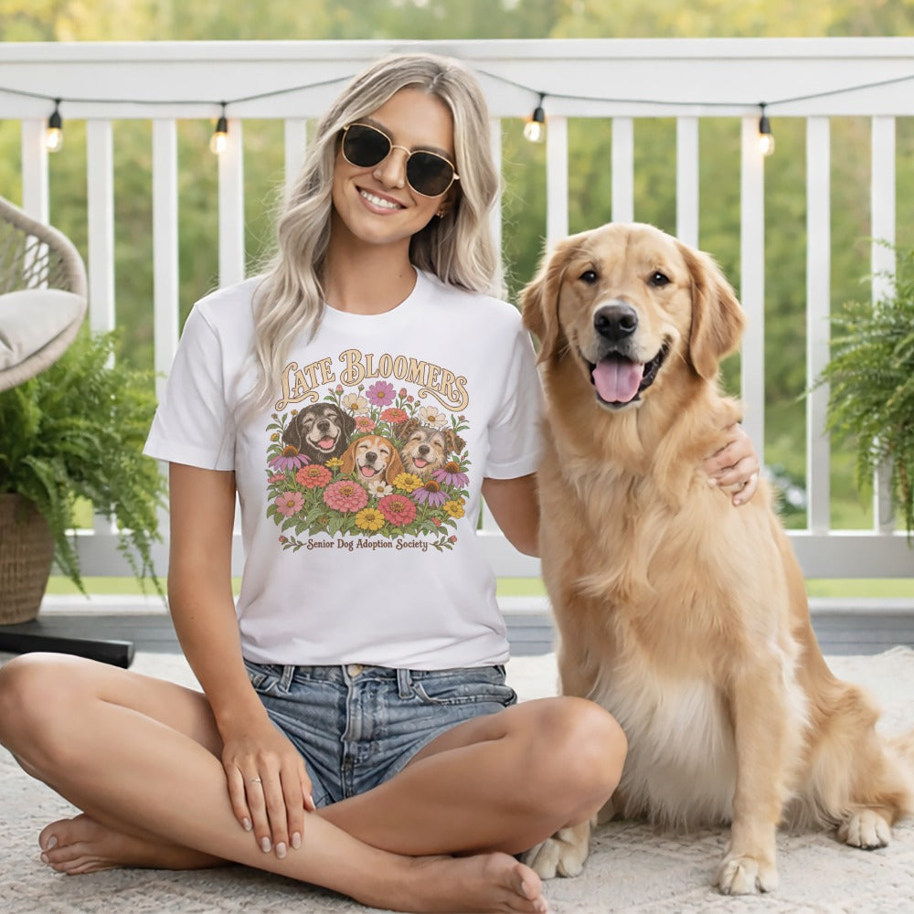A blonde woman wearing a white graphic t-shirt sits cross-legged beside a golden retriever.