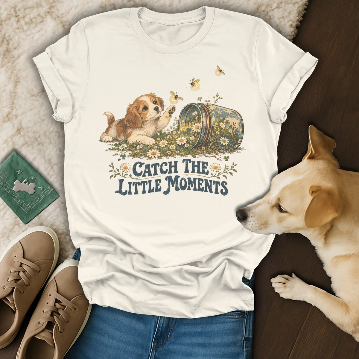 A cream graphic t-shirt with text reading Catch the Little Moments and an illustration of a puppy reaching for bees.