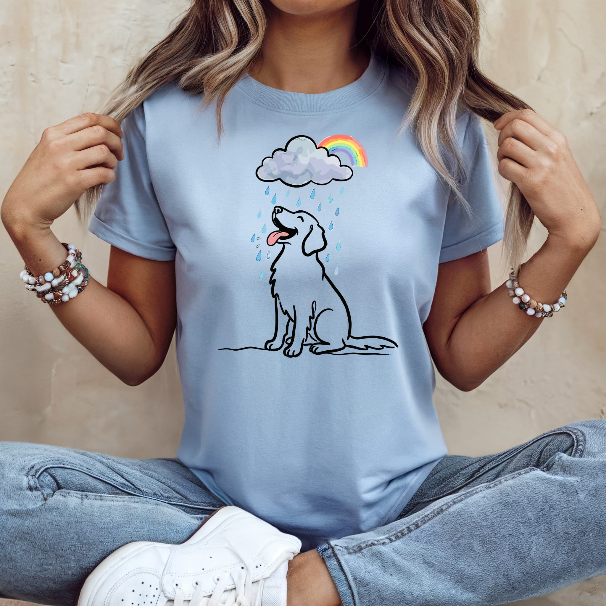 Light blue t-shirt with a cartoon dog sitting under a rainbow and rain cloud.