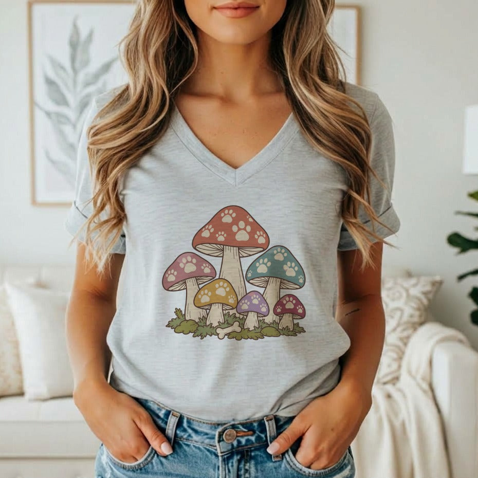 A woman wearing a gray V-neck t-shirt featuring a retro mushroom graphic with paw print patterns.