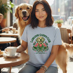 A woman wearing a light blue t-shirt with a Labrador Garden Club graphic sits with a golden retriever in a cafe.