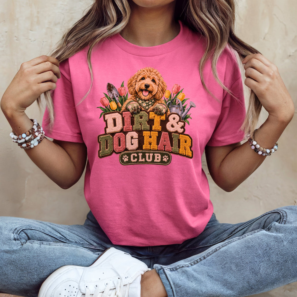 A person wearing a pink t-shirt with a graphic of a dog, flowers, and the text Dirt & Dog Hair Club.