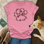 Pink t-shirt with black floral paw print design and dog nearby.