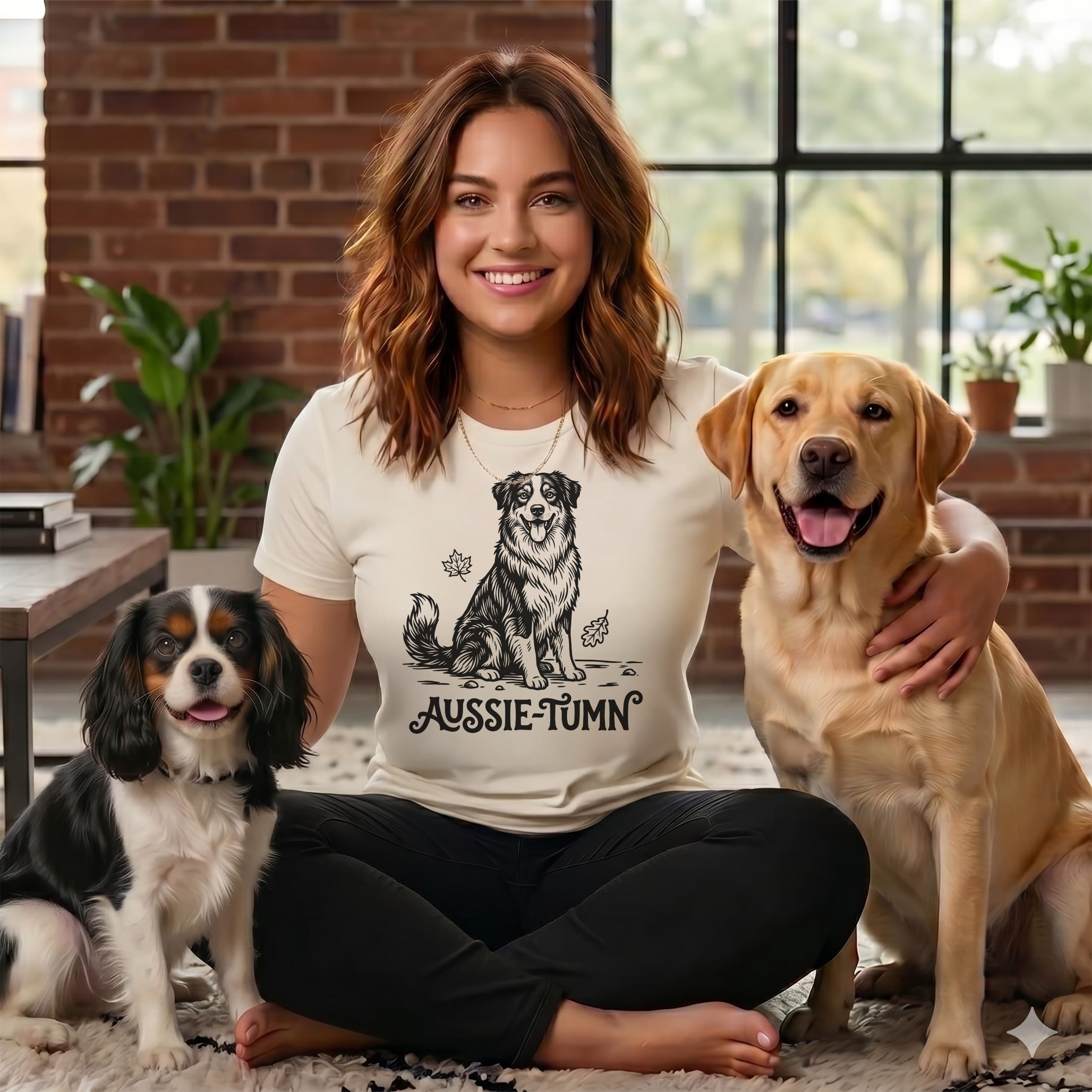 Woman with two dogs, shirt has dog graphic and text AUSSIE-TUMN.