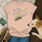 Peach t-shirt with colorful paw print flowers and a rainbow gardening trowel design.