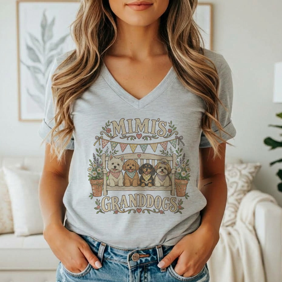 A woman wearing a gray V-neck t-shirt featuring a graphic of four dogs on a bench and the text MIMIS GRANDDOGS.
