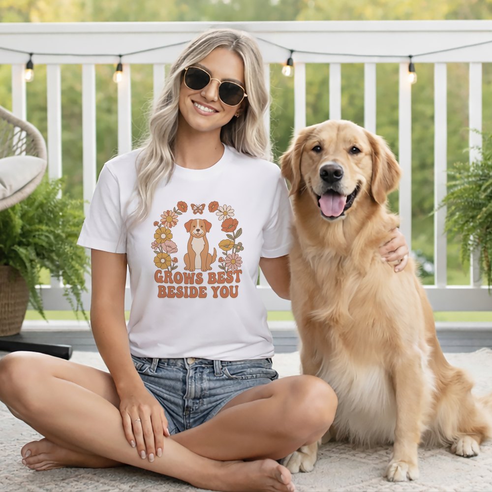 A smiling woman wearing a white t-shirt and sunglasses sits on a porch with her golden retriever.
