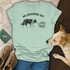 Light green t-shirt with illustration of dog facing chickens and text "NO CHICKENING OUT."