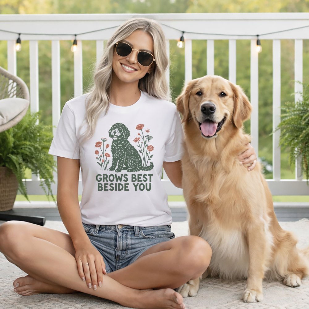 Blonde woman wearing a graphic t-shirt and sunglasses, sitting on the floor beside a golden retriever.