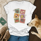A white t-shirt featuring a vintage stamp-style dog graphic with a dog, shoes, and passport nearby.