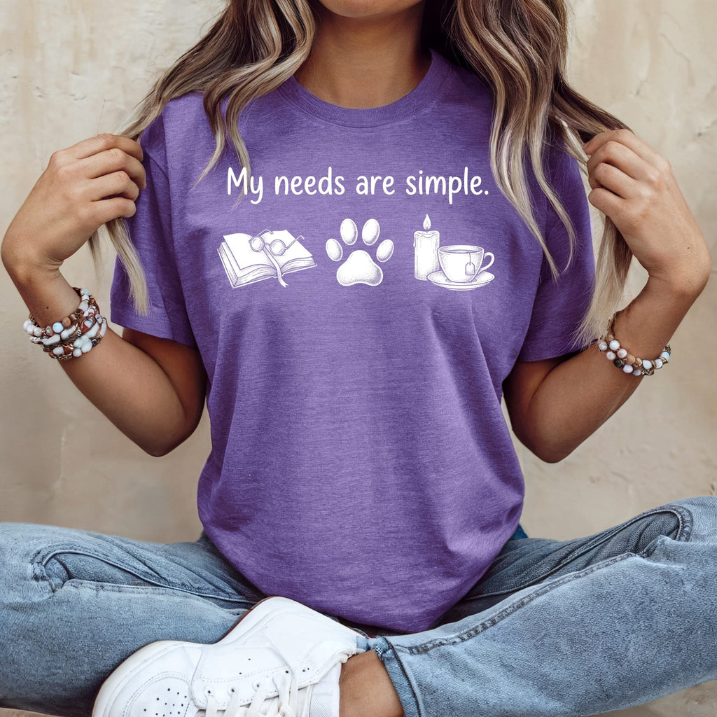 Purple t-shirt with "My needs are simple." text and book, paw print, candle, tea icons.