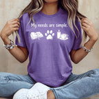 Purple t-shirt with "My needs are simple." text and book, paw print, candle, tea icons.