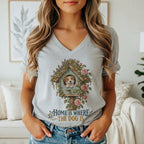 A person wearing a grey V-neck t-shirt featuring a graphic of a puppy in a birdhouse, surrounded by flowers, with the text "Home is where the dog is."