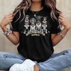 Four dogs wearing American flag bandanas sit in a row on a black t-shirt.