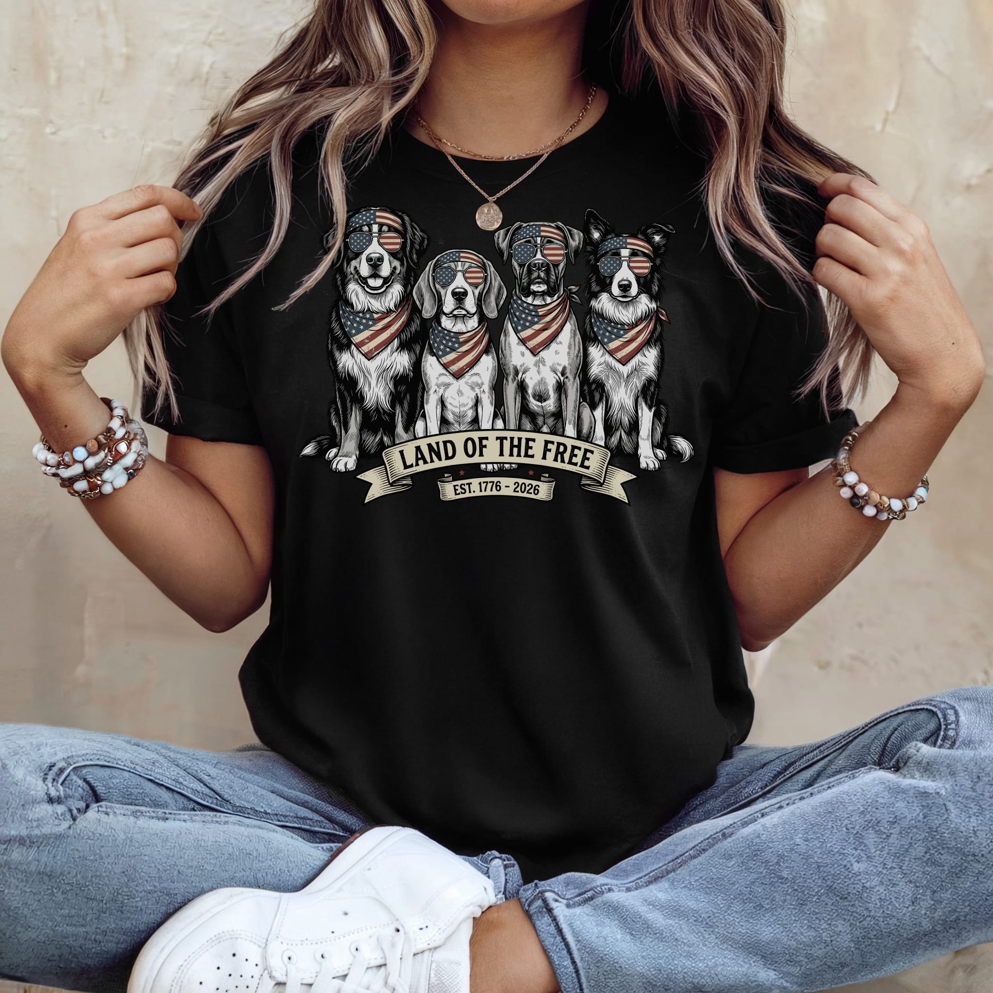 Four dogs wearing American flag bandanas sit in a row on a black t-shirt.
