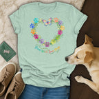 Light green t-shirt with a heart-shaped floral wreath of colorful paw prints and a butterfly, text reads "Grow Wild, Love Dogs."