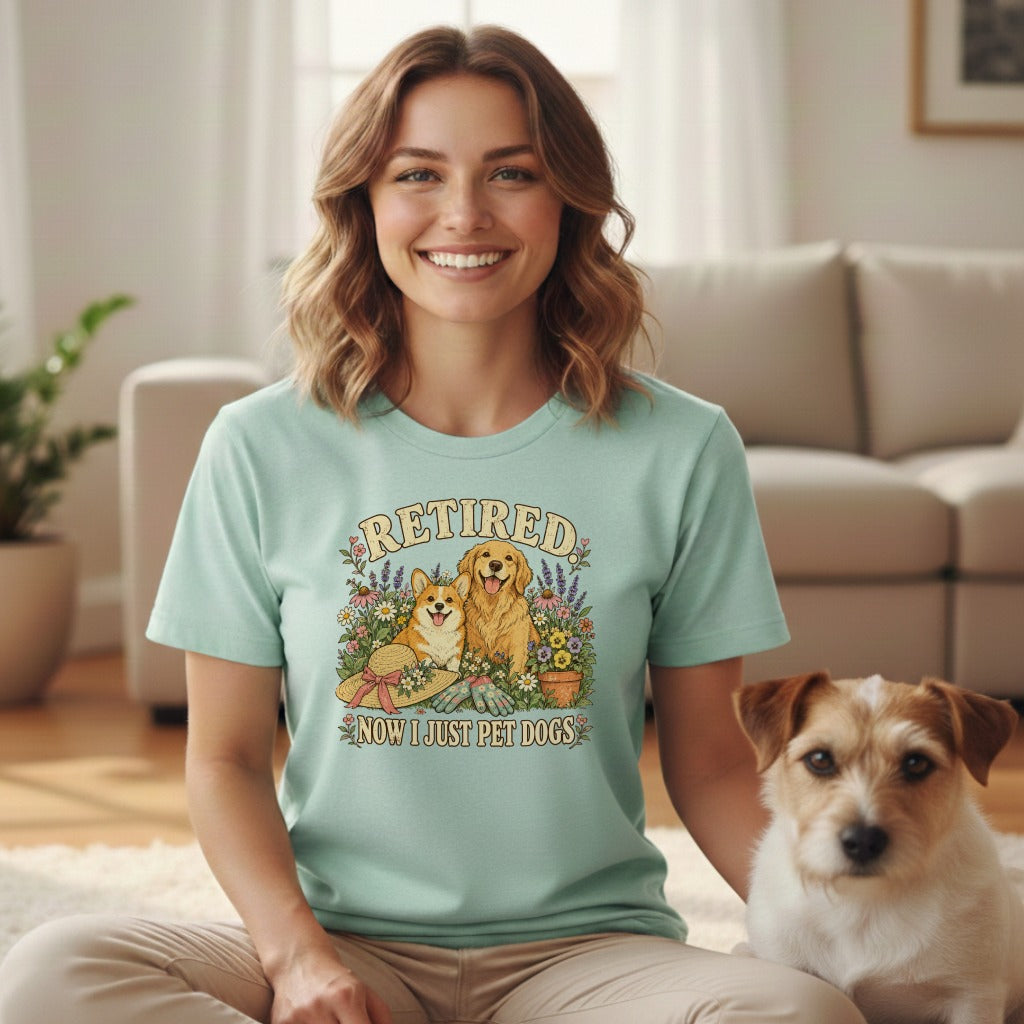 A smiling woman wearing a mint-green t-shirt with a dog graphic and text reading RETIRED NOW I JUST PET DOGS, sitting beside a terrier in a living room.