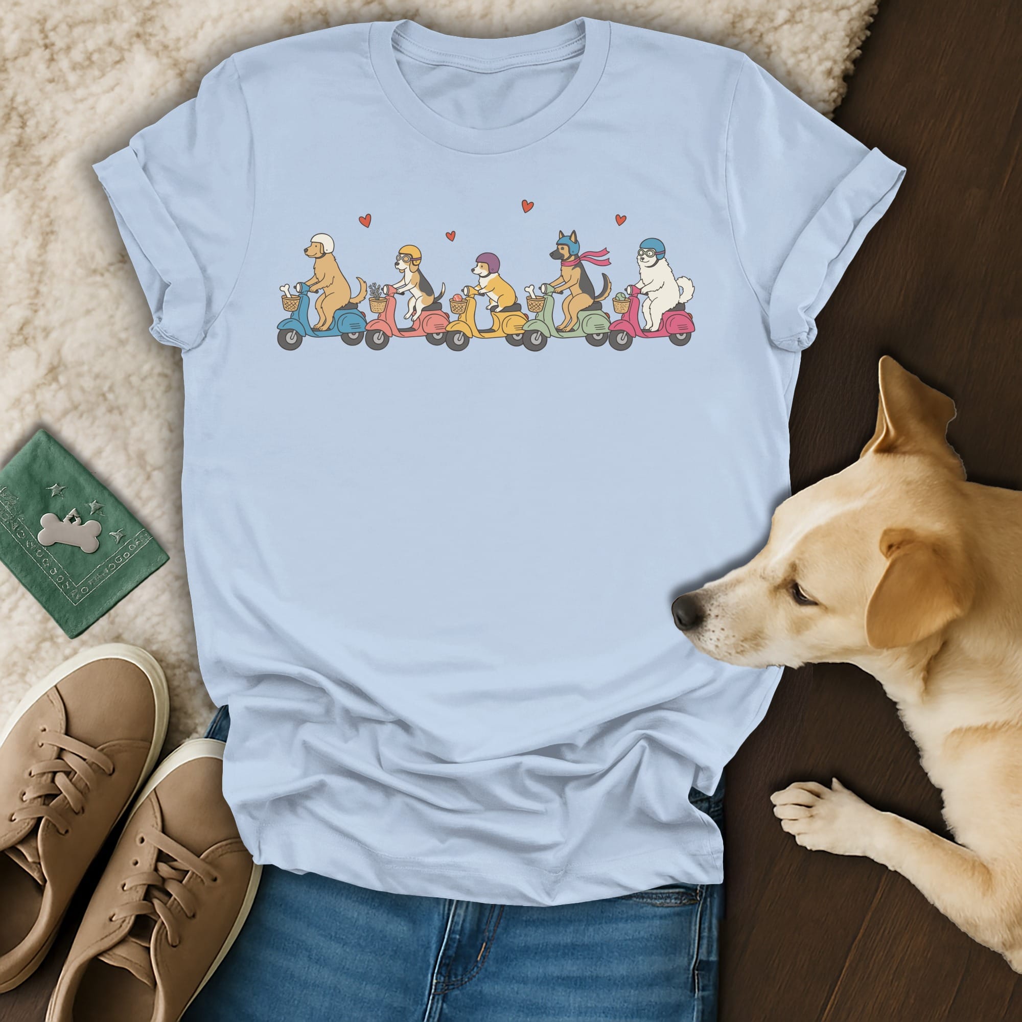 Light blue t-shirt with a line of cartoon dogs riding colorful scooters and wearing helmets.