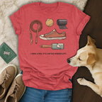 Red t-shirt with dog leash, ball, shoe, and lint roller graphic, and text.