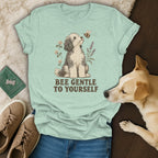 Light green t-shirt featuring a dog graphic, flowers, a bee, and the text Bee Gentle to Yourself.