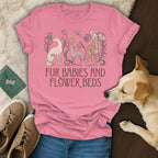 A pink t-shirt with greyhound dogs and flowers printed on the front rests on a surface next to a real dog, sneakers, and a green passport.