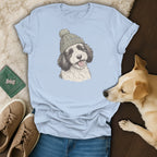 Light blue t-shirt with a sketch of a Bernedoodle wearing a knit hat.