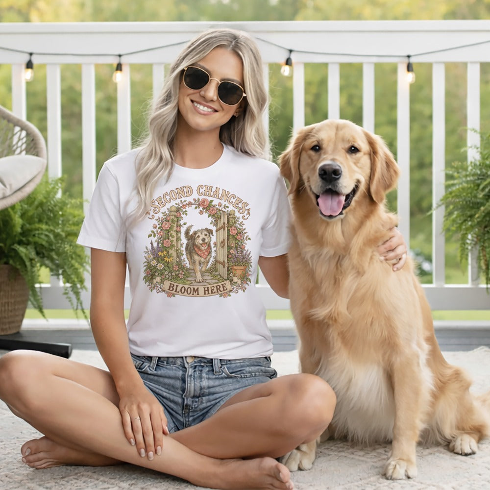 A blonde woman in a graphic tee and sunglasses sits cross-legged next to a golden retriever on a porch.