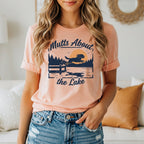 Peach t-shirt with graphic of dog jumping into lake, "Mutts About the Lake".