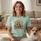 A smiling woman wearing a mint-green t-shirt featuring a dog graphic that reads "Aged to Perfection" sits next to a small dog on a rug.