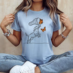 Line art of a dog chasing butterflies with a net on a light blue t-shirt.