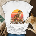 A white v-neck t-shirt featuring a retro graphic of an Australian Shepherd, flowers, and the text Aussie Mom.