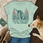 Light green t-shirt with a vintage-style dog graphic and the text FOLLOW YOUR NOSE TO THE FLOWERS.