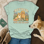 Light green t-shirt with a vintage graphic of dogs, flowers, and the text Retired Now I Just Pet Dogs.