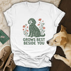 A white v-neck t-shirt featuring a green doodle dog graphic and the text GROWS BEST BESIDE YOU.