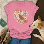 Pink t-shirt with a heart graphic of a dog among autumn leaves and mushrooms.