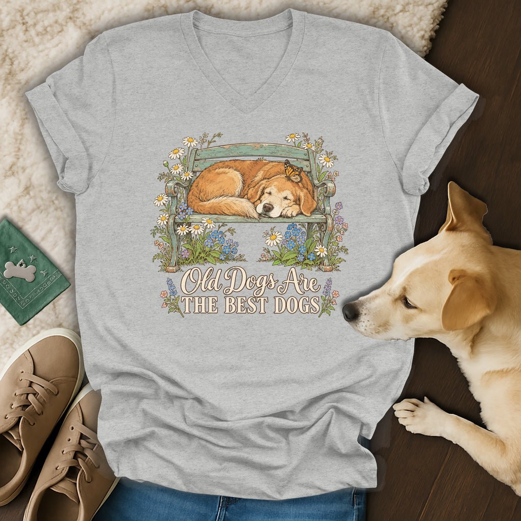 A heather gray V-neck t-shirt featuring a graphic of a sleeping golden retriever on a bench surrounded by flowers, with the text Old Dogs Are The Best Dogs.