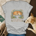 A heather gray V-neck t-shirt featuring a graphic of a sleeping golden retriever on a bench surrounded by flowers, with the text Old Dogs Are The Best Dogs.