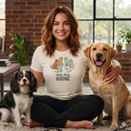 Woman in cream shirt with "dog, dog, GOOSE" text and cartoon dogs, with a labrador and spaniel.