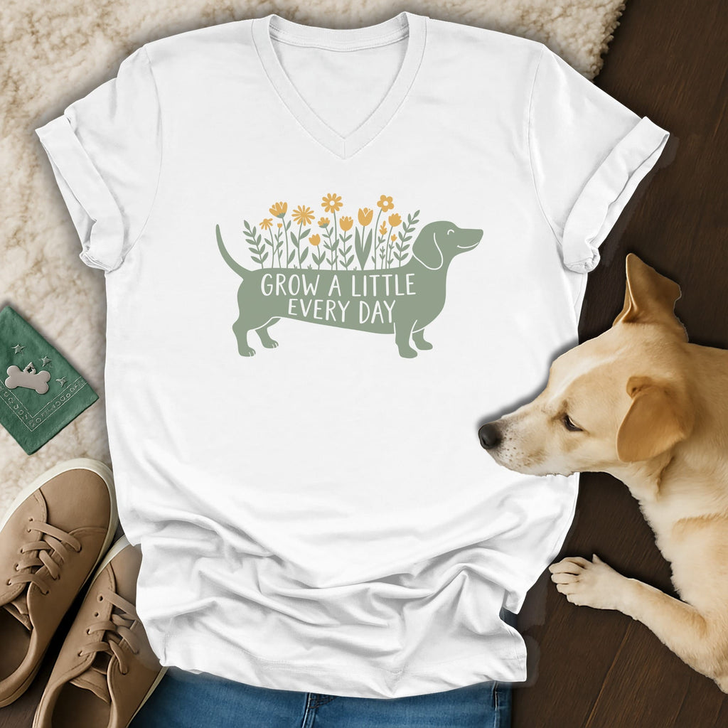 White V-neck t-shirt with a green dachshund graphic, yellow flowers, and the text Grow a Little Every Day.