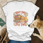 White V-neck t-shirt featuring a cartoon golden retriever playing with yarn and the text Knit One Pet Two.