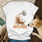 White V-neck t-shirt featuring a dachshund graphic, flowers, a watering can, and the text GROW THROUGH WHAT YOU GO THROUGH.