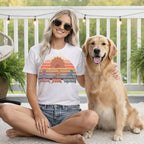 Woman wearing a "Paws, Pose, Repeat" t-shirt sits with a golden retriever.