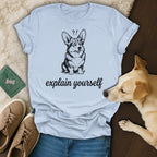 Corgi with question marks above head, "explain yourself" text, light blue t-shirt.