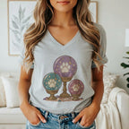 A woman wears a grey V-neck t-shirt featuring a graphic of three glowing paw print crystal balls.