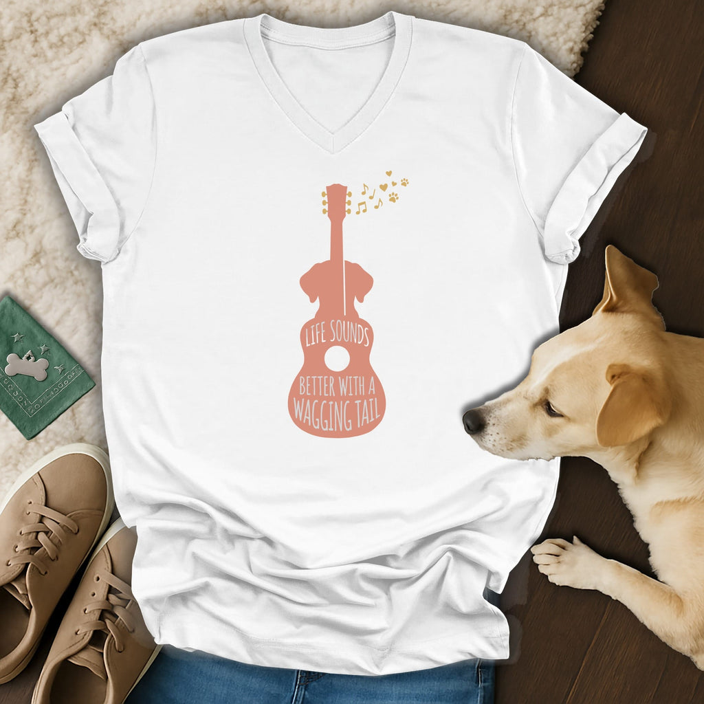 A white V-neck t-shirt featuring a pink guitar silhouette with the text LIFE SOUNDS BETTER WITH A WAGGING TAIL.